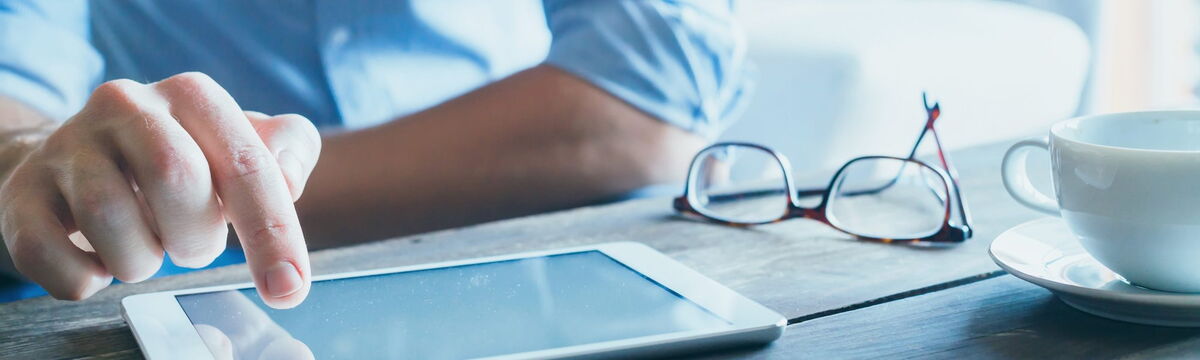 Mann liest am Tablet mit Kaffeetasse