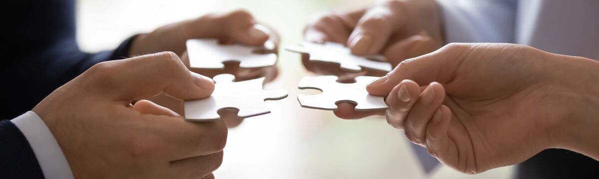 Händer von vier Menschen stecken ein Puzzle zusammen